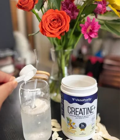 Person adding powder to a glass with flowers and a creatine supplement container in the background.